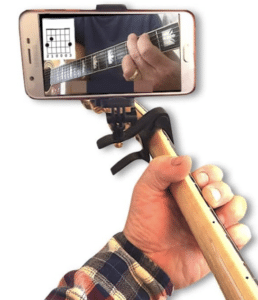 Close-up of a person holding a guitar neck with a capo and smartphone attached, displaying a chord diagram on the screen—a perfect gift idea for musicians seeking inspiration.